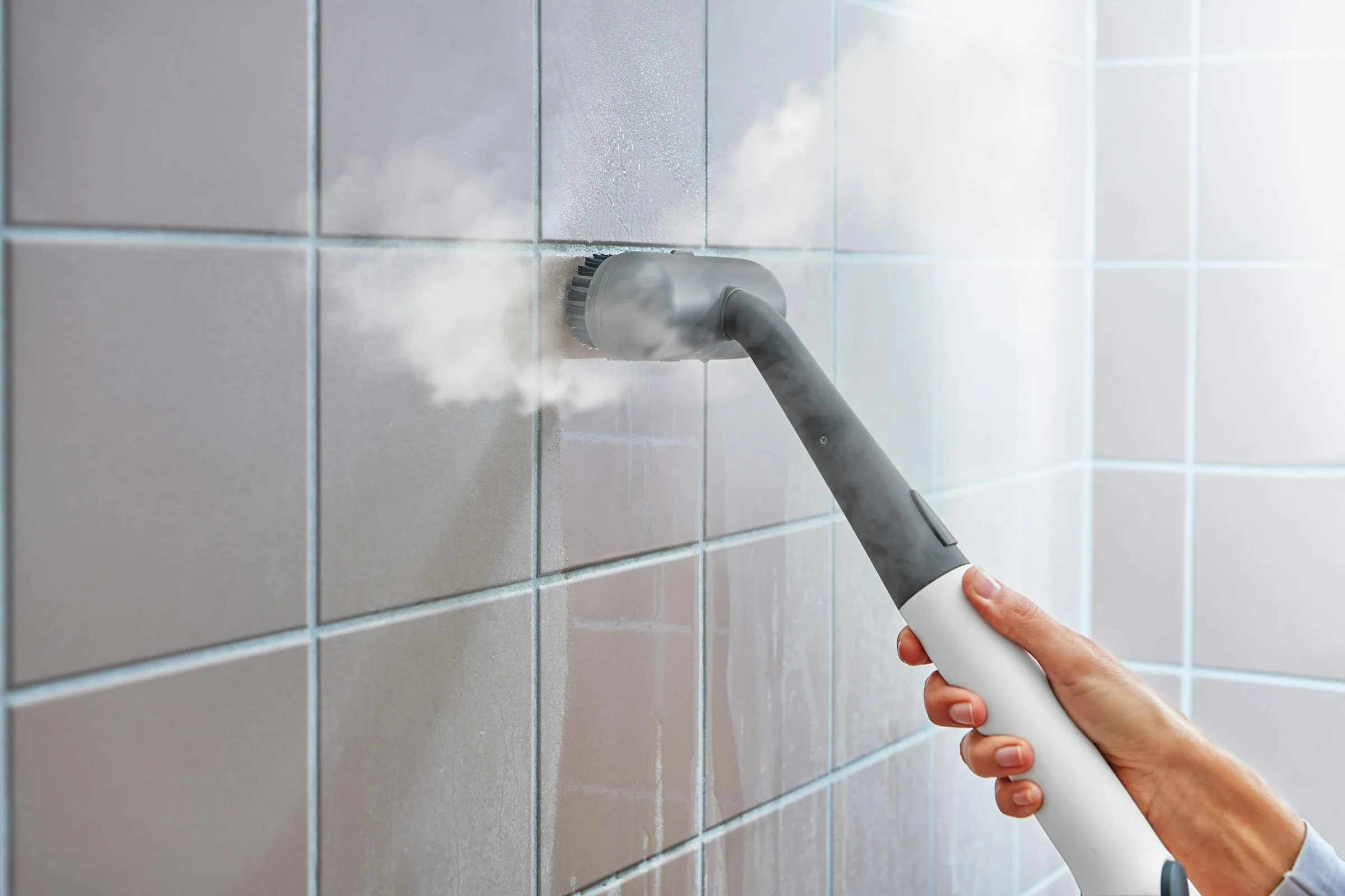 Steam cleaner nozzle lifting grime from bathroom tiles and grout